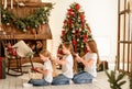 Three pretty young girls are sitting on the floor near the Christmas tree and doing each other's hair. Christmas. New Year. Royalty Free Stock Photo