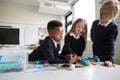 Three primary school children standing at a table in a classroom working together with toy construction blocks, close up, low angl