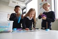 Three primary school children working together with toy construction blocks in a classroom, the girl reading instructions from a b Royalty Free Stock Photo