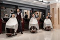 Barbers standing near clients covered with capes and sitting in hairdresser chairs. Royalty Free Stock Photo