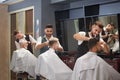 Three professional barbers trimming, cutting and styling male clients` hair. Royalty Free Stock Photo