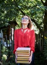 Three-quarter portrait of young blond woman, wearing eyeglasses, holding a bunch of books. Student with books in the park. Royalty Free Stock Photo