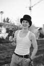 Three-quarter portrait of young man, wearing white top and black classic hat, holding sunglasses, smiling, laughing. Black and Royalty Free Stock Photo