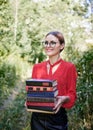 Three-quarter portrait of young woman, wearing eyeglasses with tied hairstyle, holding a bunch of books. Student with books in the