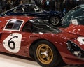 Three-quarter view of the red Ferrari 330 racecar with other cars and people in the background