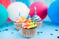 Three rainbow color cupcake with candles on blue background with colorful air balloons