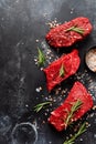 Three Raw beef steak with spices, onions and rosemary on dark slate or concrete background. Top view Royalty Free Stock Photo