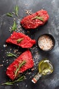 Three Raw beef steak with spices, onions and rosemary on dark slate or concrete background. Top view Royalty Free Stock Photo