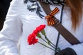 Three red carnations are in woman hands and St. George ribbon is on jacket. St. George ribbon - the symbol of the great Victory in