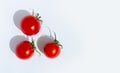 Three red cherry tomatoes with green stalks and tough shadow on a white background top view Royalty Free Stock Photo