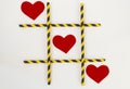 Three red felt hearts are lined up in a tic-tac-toe game, in a grid on a white background. The grid consists of colored tubes from Royalty Free Stock Photo