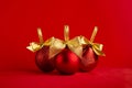 Three red glossy different christmas balls with gold shimmer bow on bright red background, copy space. Christmas background.