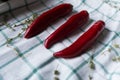 Three red hot chili peppers are lying on a draped fabric. Hurbs are used as decoration. Royalty Free Stock Photo