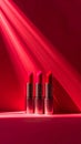 Three Red Lipsticks Lined Up On A Pink Shelf With Red Background And Dramatic Red Light Rays Royalty Free Stock Photo