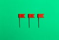 Three red little flag pins on a green background. View from above