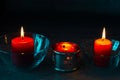 Three red paraffin candles in glass decorative candlesticks stand in a row. Bright beautiful candlelight in the dark Royalty Free Stock Photo