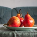 Three red pears on a green plate standing on a table covered
