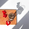 Three red poppies flowers in glass vase with water on white table and wooden background with contrast sun light and shadows close