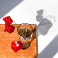 Three red poppies flowers in glass vase with water on white table and wooden background with contrast sun light and shadows close