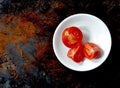 Three cut red tomatoes in a white bowl, right of center, brown background