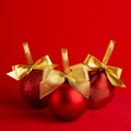 Three red shiny christmas balls with gold shimmer bow on bright deep red background, square, closeup. New year background. Royalty Free Stock Photo