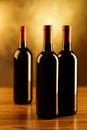 Three red wine bottles on wooden table and golden background Royalty Free Stock Photo