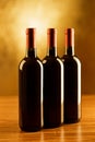 Three red wine bottles on wooden table and golden background Royalty Free Stock Photo