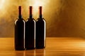 Three red wine bottles on wooden table and golden background Royalty Free Stock Photo