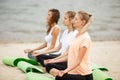 Three relaxed young girls sit in the lotus positions with closing eyes doing yoga on mats on sandy beach on a warm day Royalty Free Stock Photo