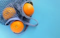 Three ripe oranges lie in a gray-blue eco-friendly string bag on a blue background