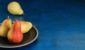 Three ripe pears in droplets of water in a ceramic plate on a blue background. Organic fruits close up. Space for text. Fresh Royalty Free Stock Photo