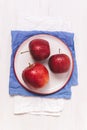 Three ripe red apples on a white plate with blue napkin. Top view on a wooden table Royalty Free Stock Photo