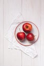 Three ripe red apples on a white plate. Top view on wooden table with a napkin Royalty Free Stock Photo