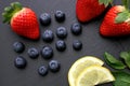 Strawberries, lemon slices, mint leaves and blueberries on black slate background Royalty Free Stock Photo