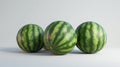 Three ripe watermelons with distinctive green stripes on a light background, showcasing their vibrant and fresh appearance