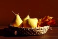 Three ripe yellow pears lie in a decorative plate with maple leaves on a wooden table, brown background, space for text Royalty Free Stock Photo