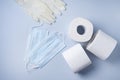 Three rolls of white toilet paper, medicine gloves and face masks on a blue background. Pandemic, covid-19, essential goods,