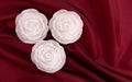 Three rose shaped candles on deep red satin