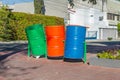Three rotating empty metal barrel trash bins on a metal base on a sidewalk in a city public garden