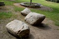 Three round boulders of gray granite lie on the lawn in the background a wooden circular bench around a tree encircles the perimet