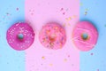 three round different sweet donuts with sprinkles on a pink-blue background