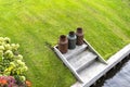 Three rusty metal milk canisters standing on the edge of the canal in the lawn.