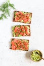 Three sandwiches with rye bread, avocado, smoked salmon on a white