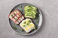 Three sandwiches on toast with cream cheese, cucumbers, quail eggs and crab sticks decorated with microgreens peas on a plate on