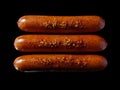 Three sausages are sitting on a black surface Royalty Free Stock Photo