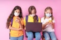 Three schoolgirls in medical masks are holding smartphones and a laptop. Distance learning concept. Back to school. Studio photo