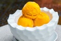 Three scoops of yellow ice cream in a white bowl on table in summer cafe. Mango flavored icy dessert Royalty Free Stock Photo