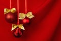 Three shimmer red balls with gold bows hang on ribbons in row on deep scarlet silky smooth wavy wall, closeup, copy space. Luxury. Royalty Free Stock Photo