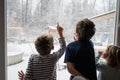 Three siblings, brothers and sister, looking out the window amazed by the snowy winter nature Royalty Free Stock Photo