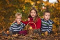 Three siblings sitting on ground in fallen leaves and eating apples from basket, brothers and sister in autumn forest, autumn Royalty Free Stock Photo